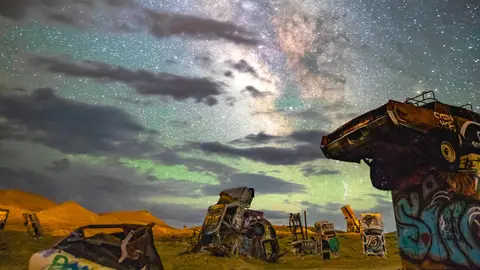 Abandoned cars stand in a field beneath a starry night sky.