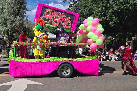 A brightly decorated parade float features a costumed character and colorful balloons.