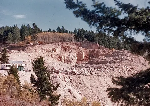 A view of an open pit quarry surrounded by pine trees.