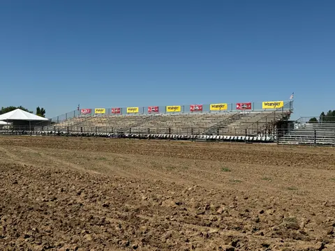 An outdoor arena with empty bleachers and a dirt field under a clear blue sky.