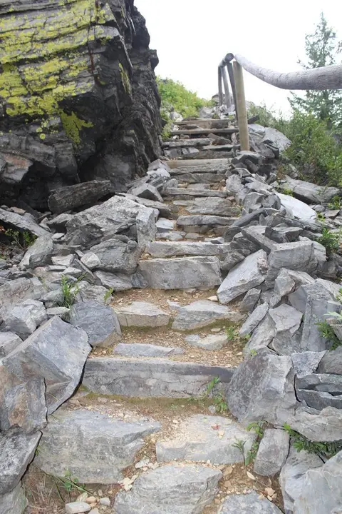 A stone staircase leads up a rocky trail alongside a cliff.