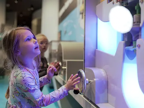 A young girl interacts with an exhibit inside a building.