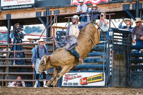 A cowboy rides a bucking bull at a rodeo.