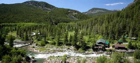 A scenic view of a river, bridge, and buildings nestled in a lush green mountain valley.
