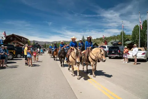 People ride horses down a street during an outdoor event with spectators.