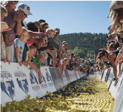A crowd of spectators watches a large mass of yellow objects rolling down a street.