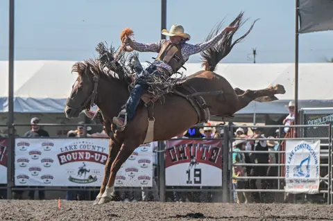 A cowboy rides a bucking horse at a rodeo arena.