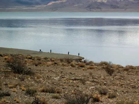 A landscape showing people fishing by a lake with mountains in the background.