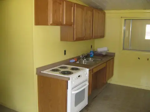 A small kitchen with yellow walls, wooden cabinets, a white stove, and a sink.
