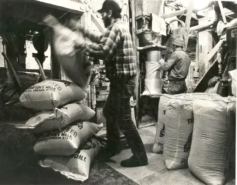 Black and white photo of workers inside a mill handling sacks of feed.