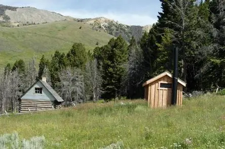A landscape view showing small cabins and a tall black chimney in a grassy mountainous area.