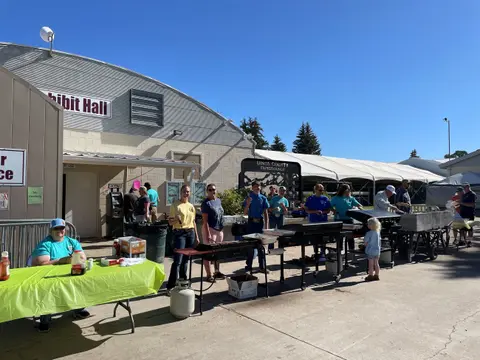 People cooking and serving food outdoors near a building with an Exhibit Hall sign.