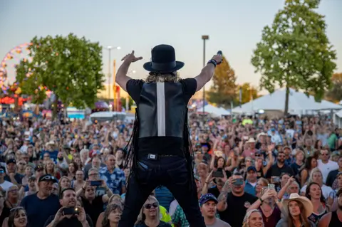 A performer faces a large crowd at an outdoor event.