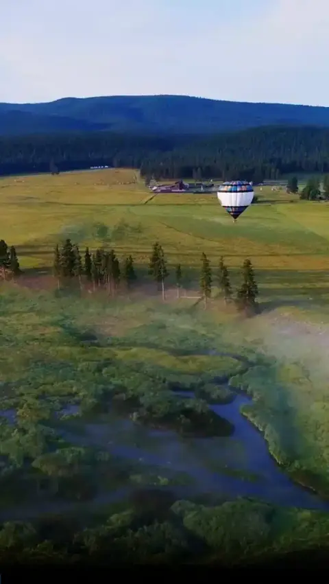 An aerial view of a hot air balloon flying over a valley and river.
