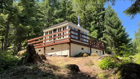 A cabin with a wraparound deck stands in a forest.