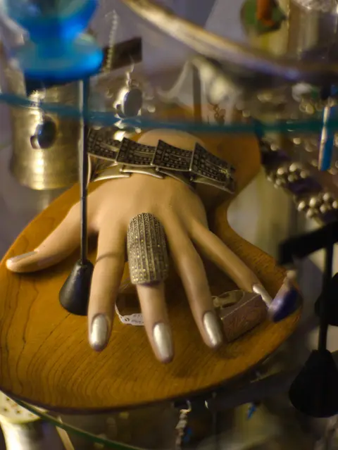 A mannequin hand displays jewelry on a wooden tray.