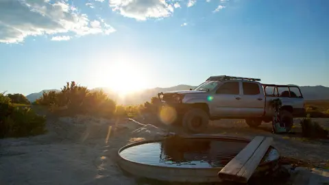 A pickup truck parked near a round water tank in a desert landscape during sunset.