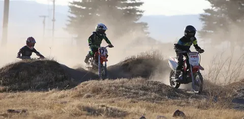 Three young dirt bike riders race across a dusty track.