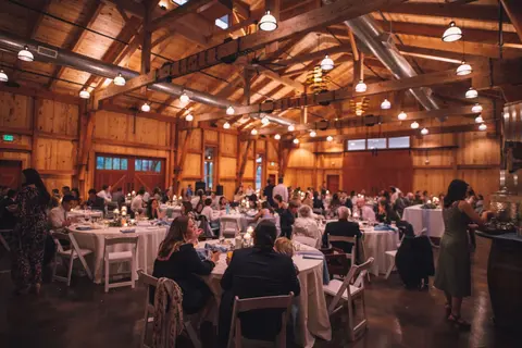 People seated at tables inside a rustic wooden barn venue for an event.