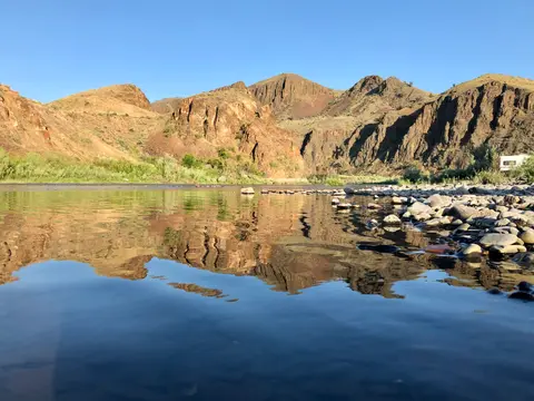 A calm river reflecting rocky hills under a clear blue sky.