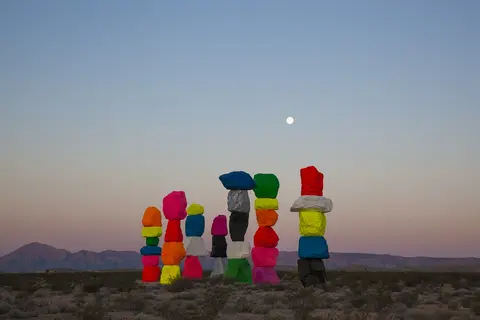 Stacks of brightly painted boulders stand in a desert landscape under a moonlit sky.