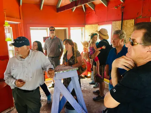 A group of people gathered inside a red-walled room with a blue wooden stand.