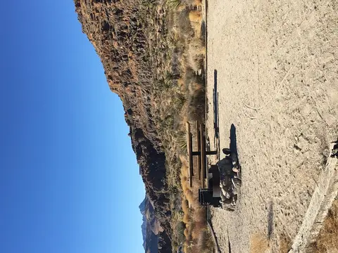 A picnic table and fire ring set against a rocky desert hillside under a clear blue sky.