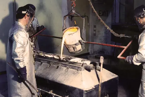 Workers pour molten metal from a crucible inside a factory.