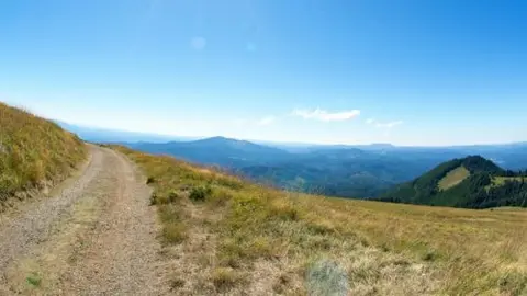 A dirt road winds along a grassy mountain ridge under a blue sky.