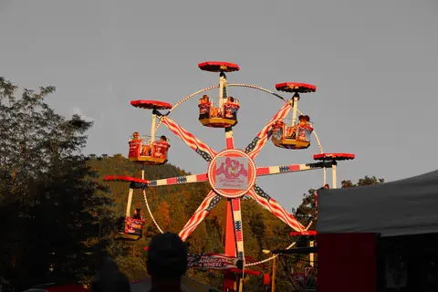 A ferris wheel decorated with American flags rotates at an outdoor event.