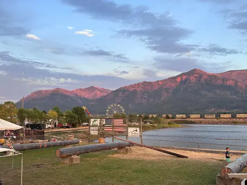 A scenic view of a fair near a river with mountains in the background at sunset.
