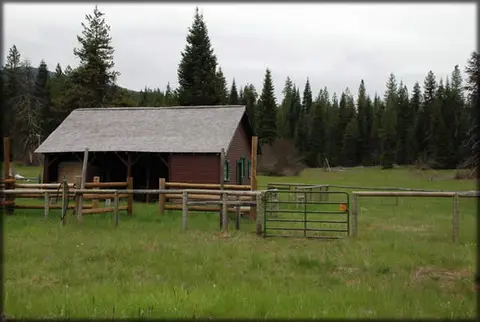 A red barn stands in a grassy field surrounded by trees.