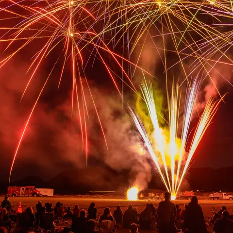 A crowd watches fireworks lighting up the night sky over a field.