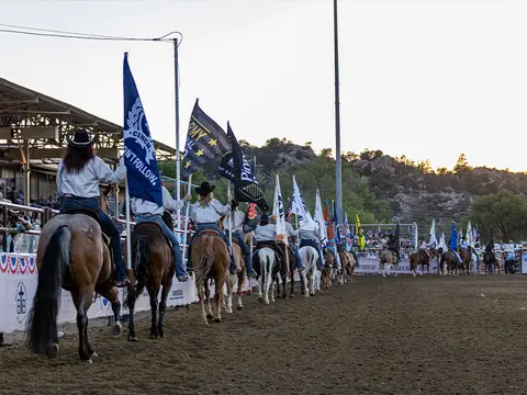 A line of horseback riders carrying flags in an arena.