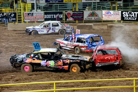 Several heavily damaged cars participate in a demolition derby event on a dirt track.
