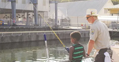 A child fishing with an instructor by a water basin.