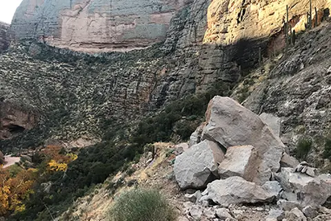 Large boulders fallen on a steep mountain path with cliffs in the background.