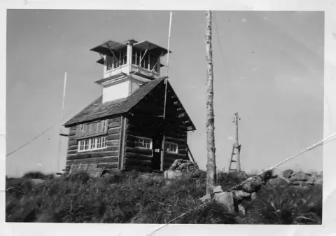 Black and white photo of a log structure with an observation tower on top.