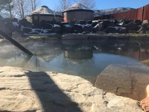 A hot spring pool with yurts and mountains in the background.