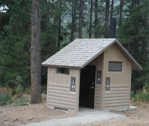 A small, modern public restroom building stands in a wooded area.
