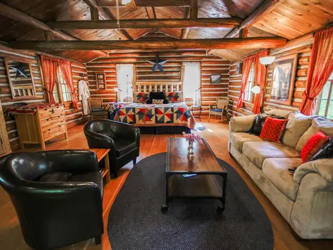 A rustic log cabin interior with a bed, seating area, and wooden ceiling.