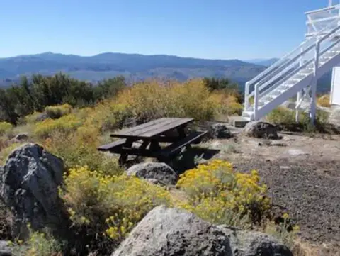 A wooden picnic table sits on a hilltop with mountains in the background.