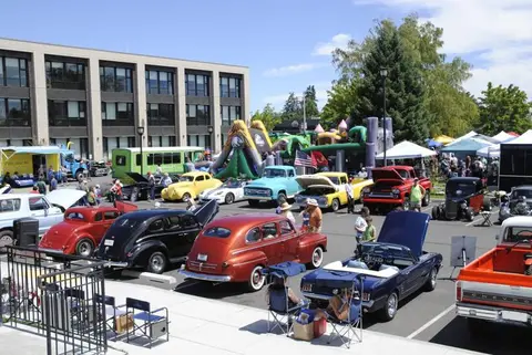 A car show and outdoor event with classic cars and people gathered in a parking lot.
