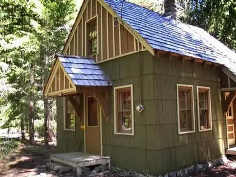 A small cabin stands among trees in a forest.