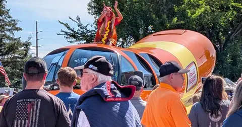 A hot dog-shaped vehicle is at an outdoor event with people around it.