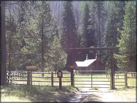 A cabin nestled behind a fence and gate in a forest.