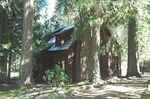 A rustic wooden cabin surrounded by tall trees in a forest.