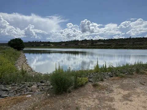 A calm lake reflecting fluffy white clouds under a blue sky.