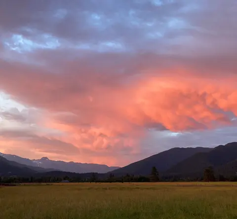 A sunset glows brightly over a field and mountain range.