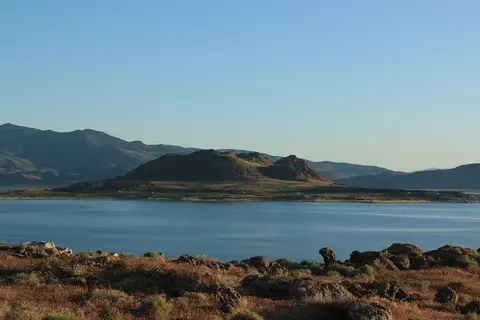 A wide shot of a lake with an island and mountains under a clear sky.